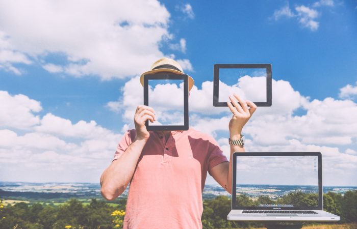 man-standing-in-meadow-holding-digital-tablet-with-laptop-in-foreground-2