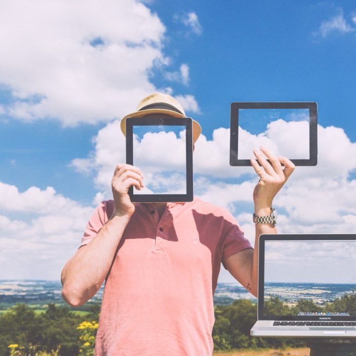 man-standing-in-meadow-holding-digital-tablet-with-laptop-in-foreground-2